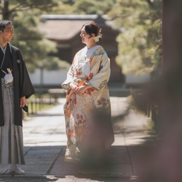 松並木の参道で見つめ合う、羽織袴の新郎と花柄の色打掛の花嫁。趣ある建物を背景にした三渓園の結婚写真
