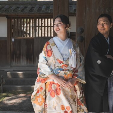 三溪園にて、重厚な木戸を背に遠くを見上げる色打掛の花嫁と、腕を組む黒紋付袴の新郎。凛とした雰囲気の和装前撮り