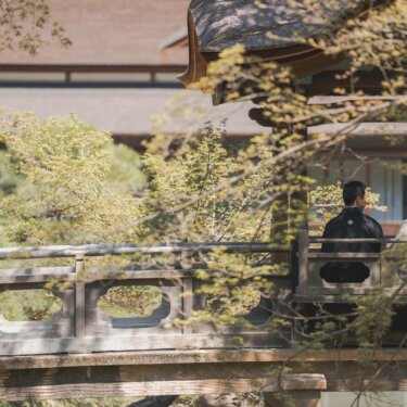 木漏れ日に包まれた石橋の欄干越しに、並んで佇む新郎新婦の後ろ姿を写した和装フォトウェディング