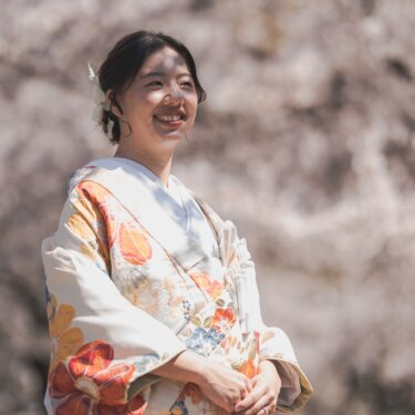 満開の桜を背景にほほえむ、花柄の色打掛の花嫁のソロショット。白い髪飾りがやさしい和装前撮り