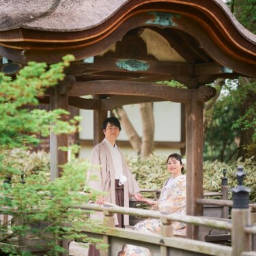 唐破風の東屋の橋で、カメラに笑顔を向ける羽織袴の新郎とベンチに座る色打掛の花嫁。三渓園の緑に囲まれた前撮り