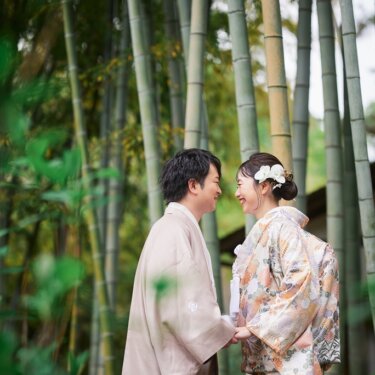 竹林の中で手を取り合い、大笑いしながら見つめ合う新郎新婦。前景の葉をぼかした和装ロケーションフォト