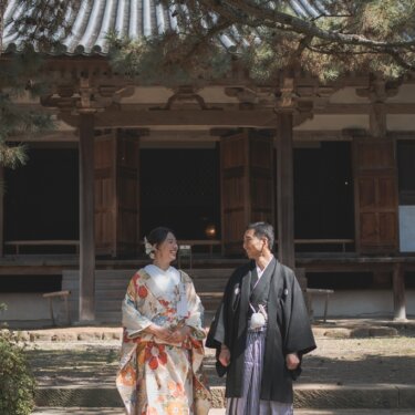 瓦屋根の古いお堂の石段の前で見つめ合う、色打掛の花嫁と羽織袴の新郎。歴史ある建物で撮る和装フォトウェディング