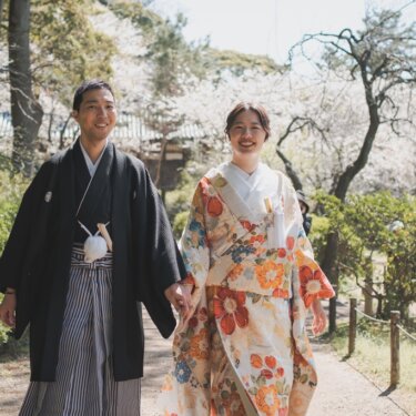 満開の桜が咲く小径を手をつないで歩く、黒紋付袴の新郎と花柄の色打掛の花嫁。三渓園で撮る和装前撮り