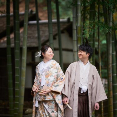 三渓園の竹林と茅葺屋根の建物を背景に、ほほえみ合う色打掛の花嫁と羽織袴の新郎。落ち着いた色合いの和装前撮り