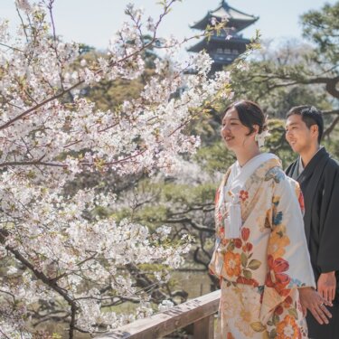 桜の枝の向こうに三重塔が見える橋の上で、花を眺めてほほえむ色打掛の花嫁と新郎の和装前撮り