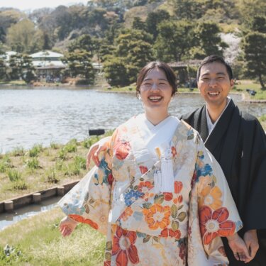 三渓園の大池のほとりで大笑いする、花柄の色打掛の花嫁と黒紋付の新郎。緑の景色と水辺を背景にした自然体の和装前撮り
