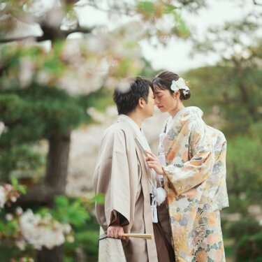桜の枝の下で額を寄せ合う色打掛の花嫁と新郎。淡い花色がやさしい春の和装フォトウェディング
