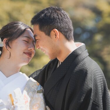 額を寄せ合い、目を閉じて笑い合う新郎新婦のアップ。白い花の髪飾りと色打掛がやさしい和装フォトウェディング