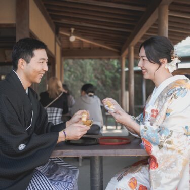 三渓園の茶屋の席で団子を手に笑い合う、黒紋付の新郎と花柄の色打掛の花嫁。食べ歩き気分で楽しむ和装前撮り