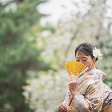 黄色い扇子で口元を隠してほほえむ色打掛の花嫁。遠くに三重塔が霞む三渓園で撮る和装前撮りのソロショット