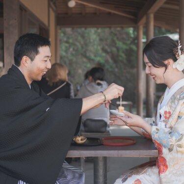 茶屋の席で新郎が花嫁に団子を食べさせる、ほほえましいシーン。色打掛で楽しむ和装フォトウェディング
