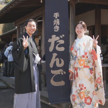 '手焼き だんご'の暖簾の前でピースサインをする、羽織袴の新郎と色打掛の花嫁。三渓園で撮る遊び心ある前撮り