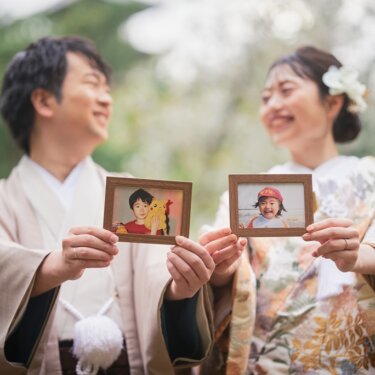 子どもの頃の写真を額に入れて見せ合い、笑い合う新郎新婦。色打掛と羽織袴で撮る家族の歴史を感じる前撮り