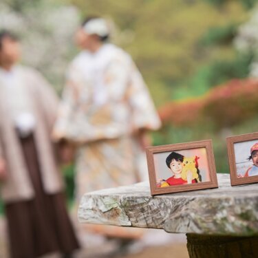 石のベンチに置いた幼少期の写真の額縁を手前に、奥の新郎新婦をぼかした演出がおしゃれな前撮り
