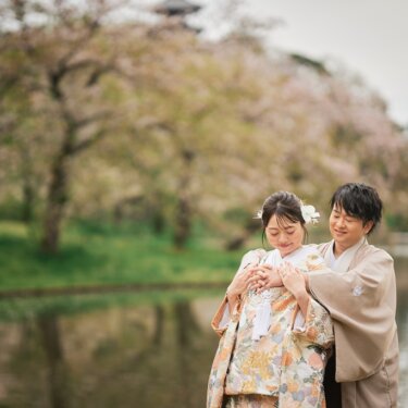 桜が水面に映る三渓園の池のほとりで、後ろから花嫁の手を包み込む新郎。色打掛で撮る春の結婚写真
