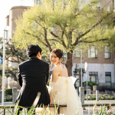 チューリップの咲く花壇と街のビル群を背景に、振り返って笑う花嫁の後ろ姿。春の横浜で撮る結婚写真