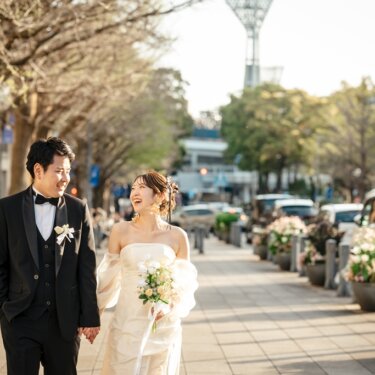 マリンタワーを望む並木道の歩道を手をつないで歩く新郎新婦。街路の花々も美しい横浜の前撮り