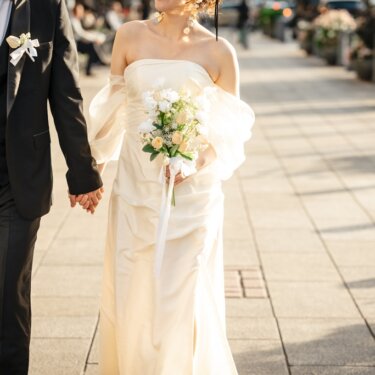 石畳の歩道を手をつないで歩く新郎新婦の胸元から下を写したカット。シャンパンベージュのドレスとブーケが美しいウェディングフォト