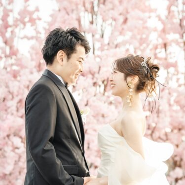 満開の桜を背に、大きなリボンのオフショルダーのドレスの花嫁と見つめ合う新郎の春の前撮り