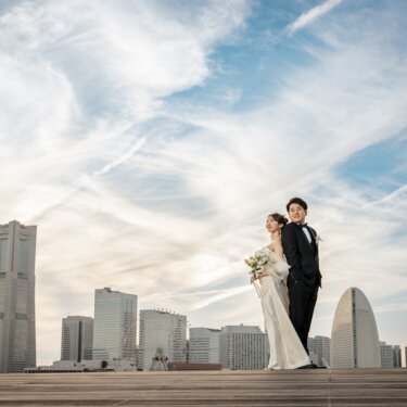 大さん橋のウッドデッキで、ランドマークタワーと観覧車を望む空を背にした新郎新婦の後ろ姿の前撮り