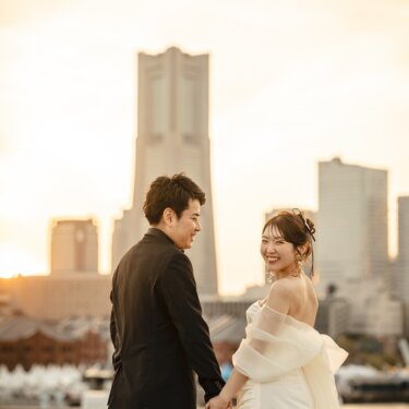 横浜ランドマークタワーの夕焼けを背景に、手をつなぎ振り返って笑う新郎新婦。大さん橋で撮るロケーションフォト