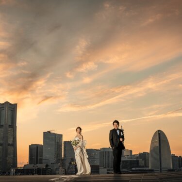 大さん橋のデッキで見つめ合う新郎新婦。ランドマークタワーと深まる夕焼けの色が美しい夕方の前撮り