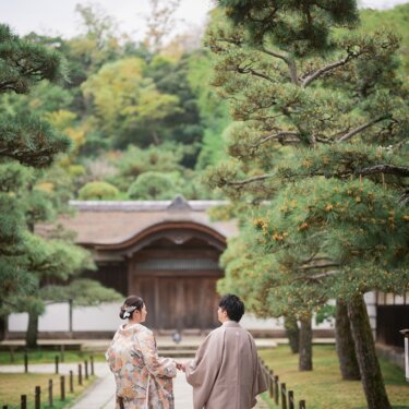 松並木の石畳の参道を、手をつないで門へ向かう新郎新婦の後ろ姿。三渓園で撮る和装フォトウェディング
