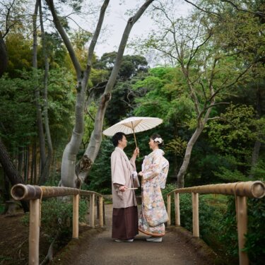 竹の手すりがある小さな橋で、白い和傘を差して見つめ合う新郎新婦。三渓園の竹林に囲まれた和装ロケーションフォト
