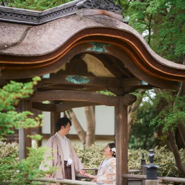 唐破風の東屋のベンチに座る色打掛の花嫁と、立って見つめる新郎。新緑がまぶしい三渓園の和装ロケーションフォト