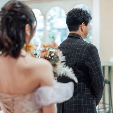 後ろ姿でアーチ窓を見つめる新郎新婦。ドレスの背中の編み上げが美しいスタジオフォト