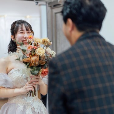 オレンジ系のドライフラワーのブーケを手に大笑いする花嫁を、新郎の背中越しに写したスタジオフォト