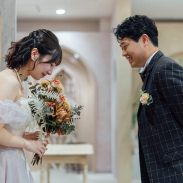 ドライフラワーのブーケに顔を寄せる花嫁を、身をかがめて見つめる新郎。スタジオで撮るファーストミートの前撮り