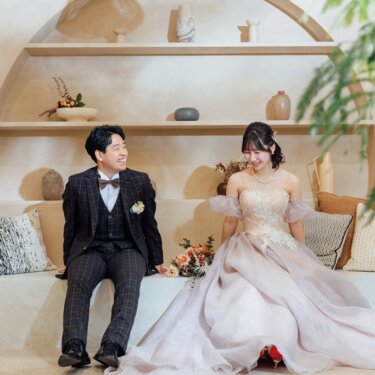ランタンの照明のアーチ棚を背に並んで座る、赤いヒールがのぞく華やかなカラードレスの花嫁と新郎のスタジオフォト
