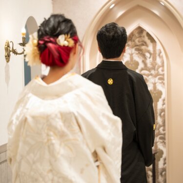 ゴシック調のアーチの入口に向かって立つ新郎新婦の後ろ姿。紋付の家紋と赤い髪飾りが印象的な和装スタジオフォト