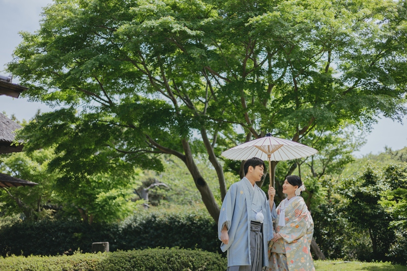 白い和傘を差して歩く和装の新郎新婦