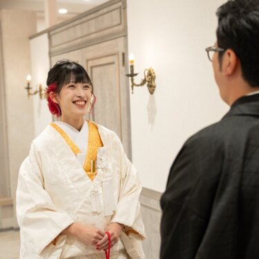 新郎の背中越しに、振り返って笑う白無垢の花嫁。色掛下の山吹色が映える和装前撮りのファーストミート