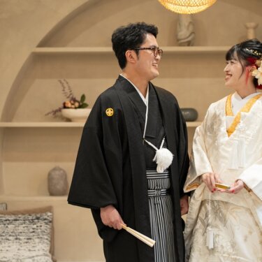 アーチ状の飾り棚の前で見つめ合って笑う紋付袴の新郎と白無垢の花嫁。明るいスタジオで撮る和装前撮り