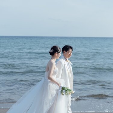 青い海を背景に、ブーケを持って並んで歩く新郎新婦。ドレスの裾が風に揺れる爽やかなビーチフォトウェディング