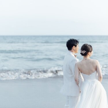 七里ヶ浜の水平線を眺める新郎新婦の後ろ姿。花嫁の髪飾りと背中のレースが美しい、海辺の前撮りのバックスタイル