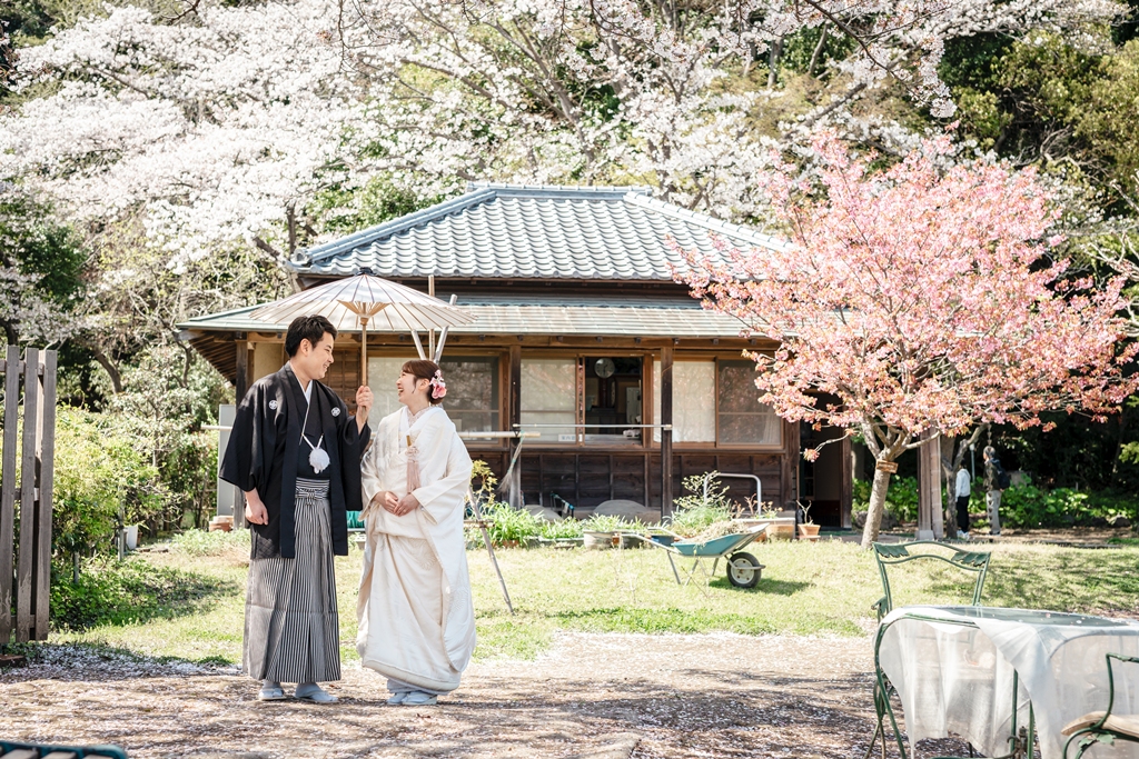 桜の木の下で和傘を差して微笑み合う新郎新婦