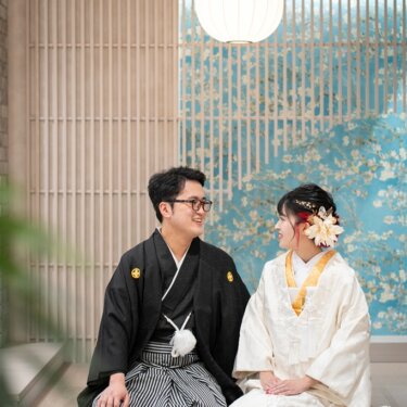 丸い和紙の照明の下、ベンチに並んで座り見つめ合う紋付袴の新郎と白無垢の花嫁。モダンな和装スタジオフォト