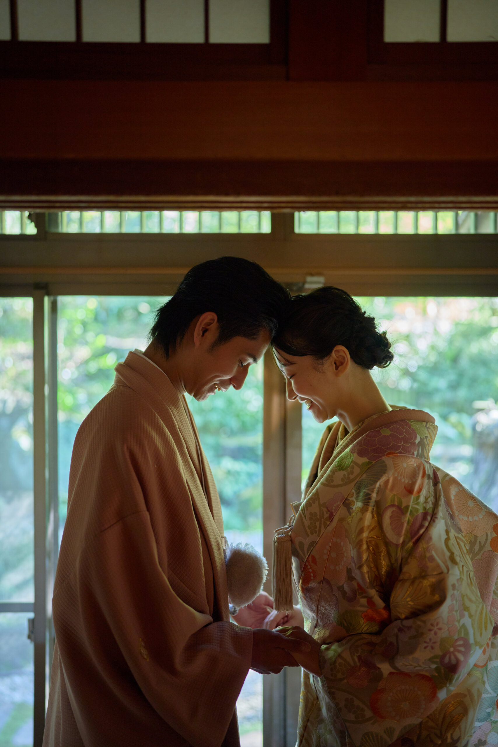 紅葉を背景に佇む淡いピンクの色打掛と羽織袴の新郎新婦