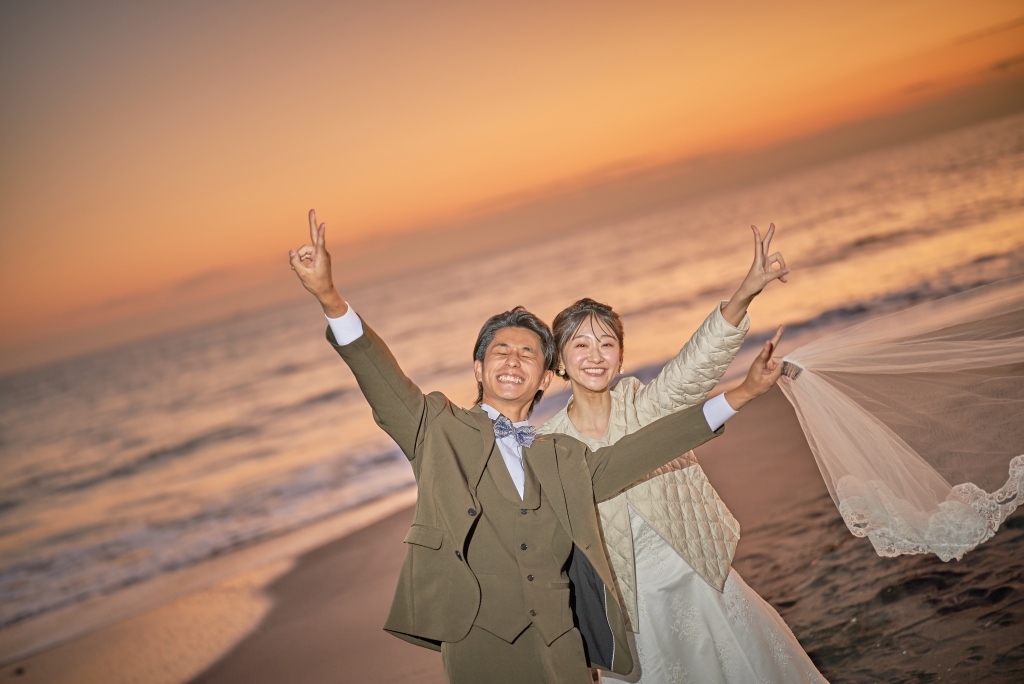 夕焼けの浜辺でピースサインをして喜ぶ新郎新婦