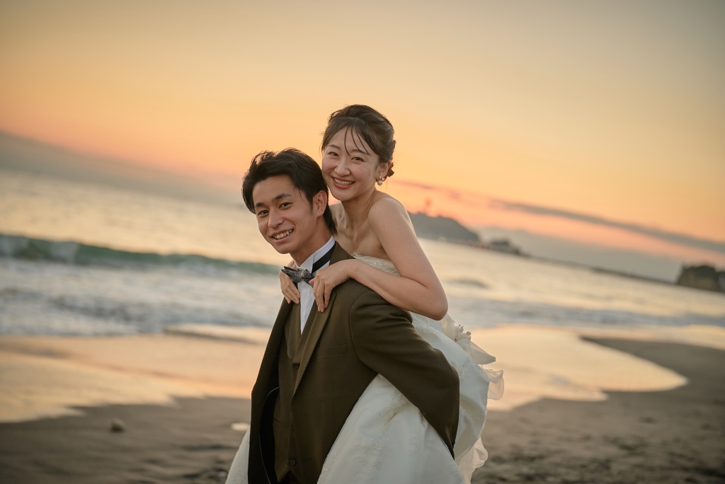 夕焼けの浜辺でおんぶをして笑い合う新郎新婦