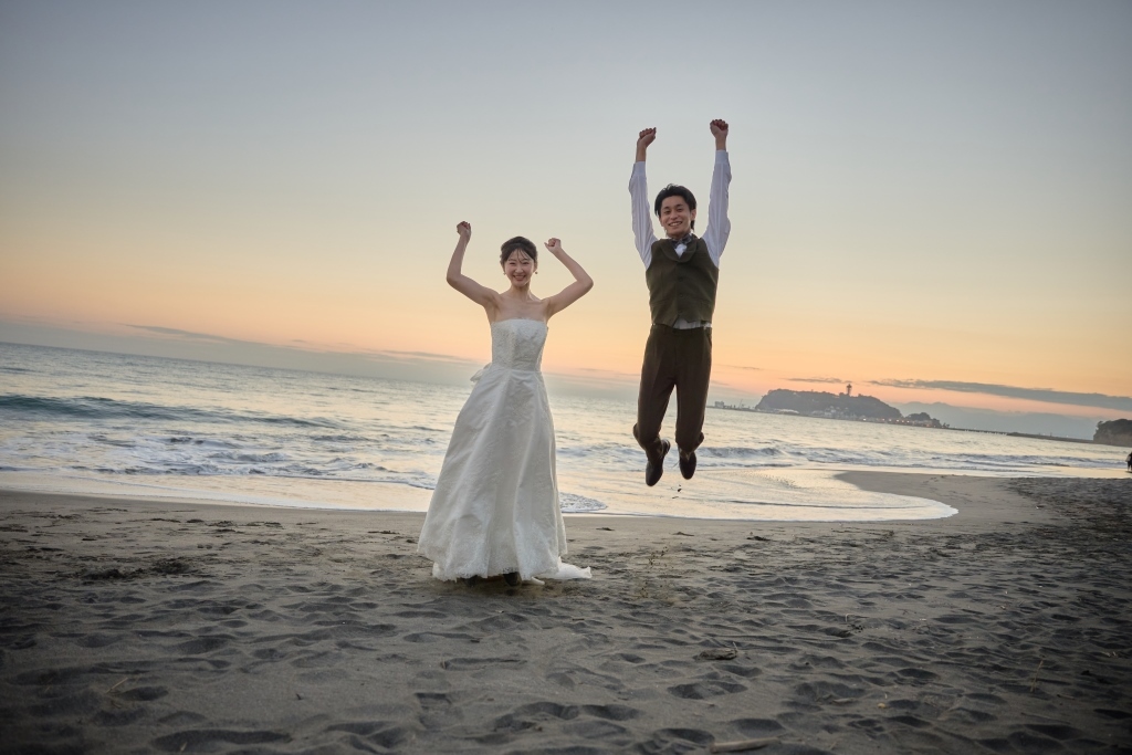 夕暮れの浜辺で両手を上げてジャンプする新郎新婦