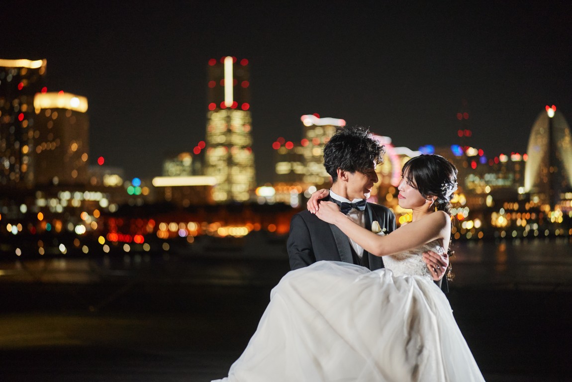 みなとみらいの夜景を背景に新郎に抱き上げられて微笑む新婦