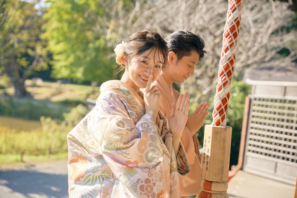 手水舎の前で手を合わせるポーズをする新郎新婦