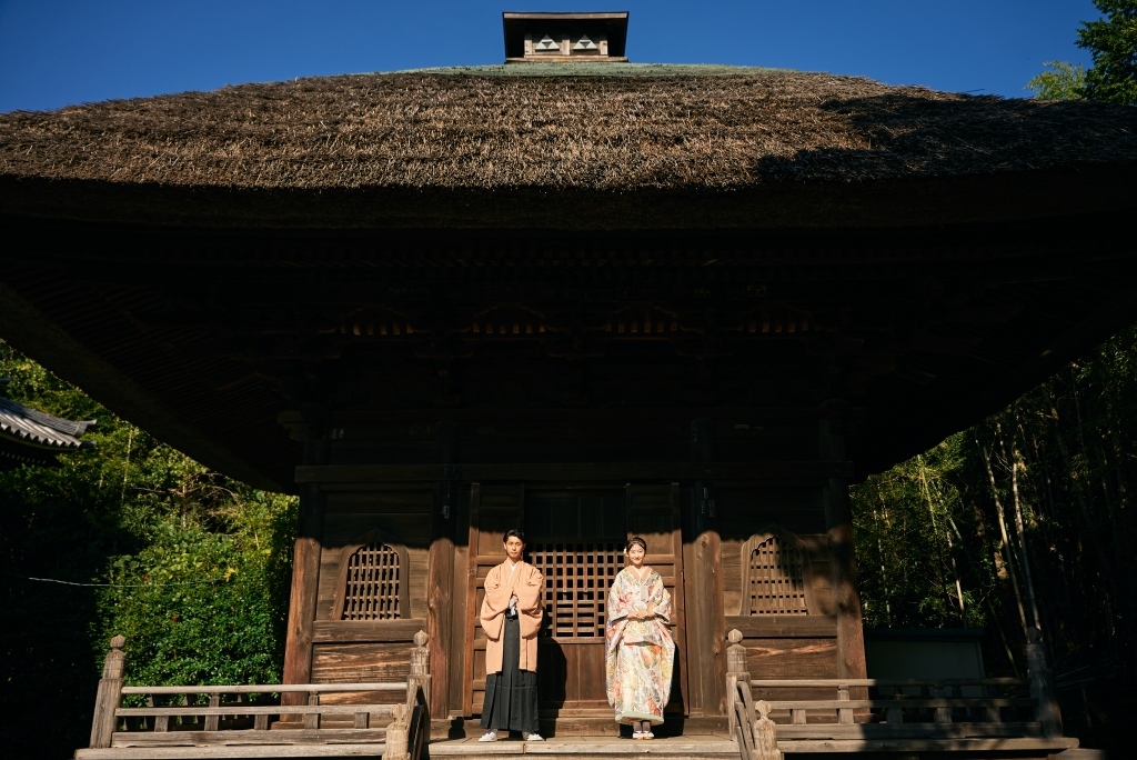 茅葺屋根の重厚な山門の前に並んで立つ和装の新郎新婦