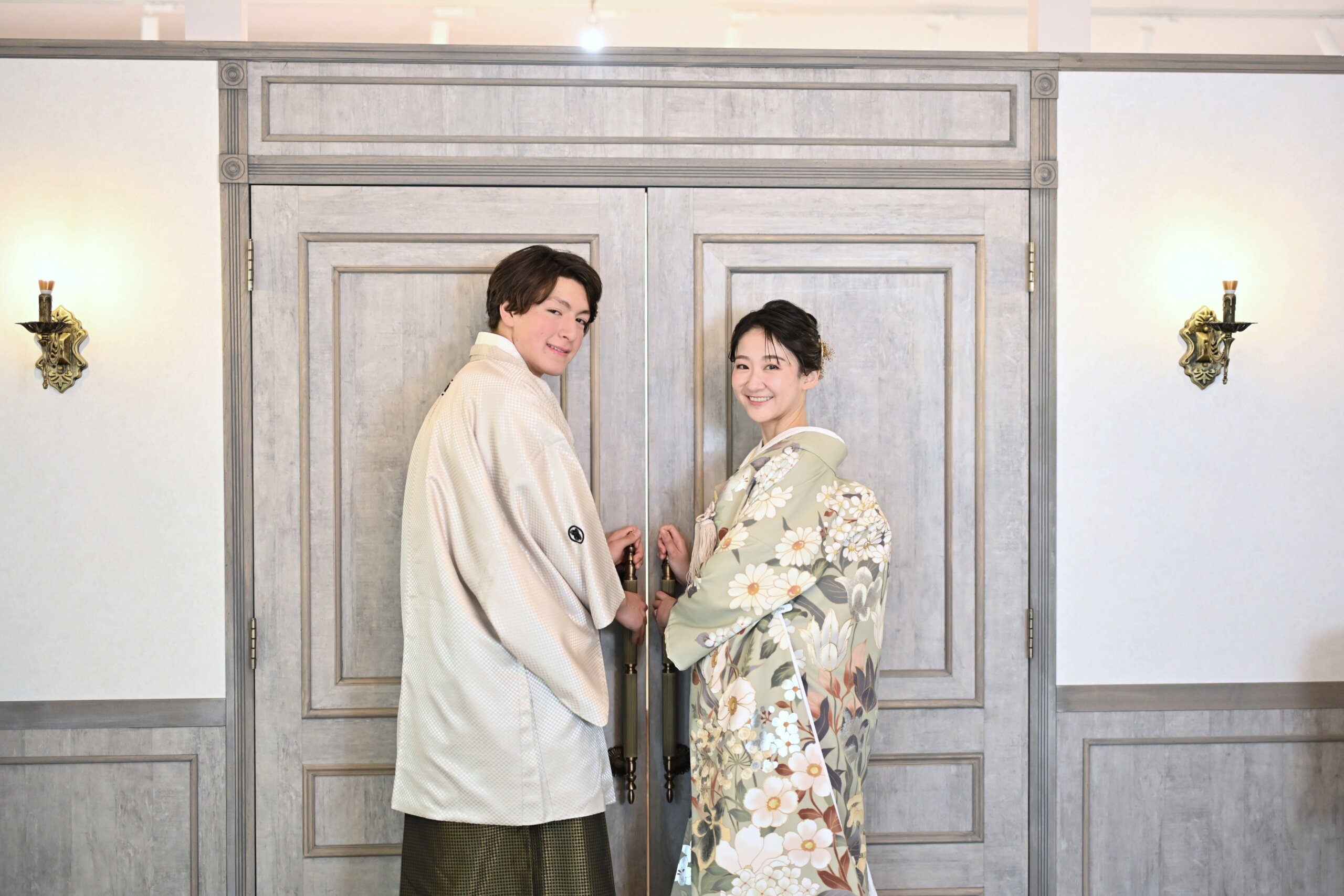 白い扉の前で手をつないで振り返るベージュの羽織袴の新郎と花柄の色打掛の花嫁。横浜店のスタジオで撮る和装前撮り